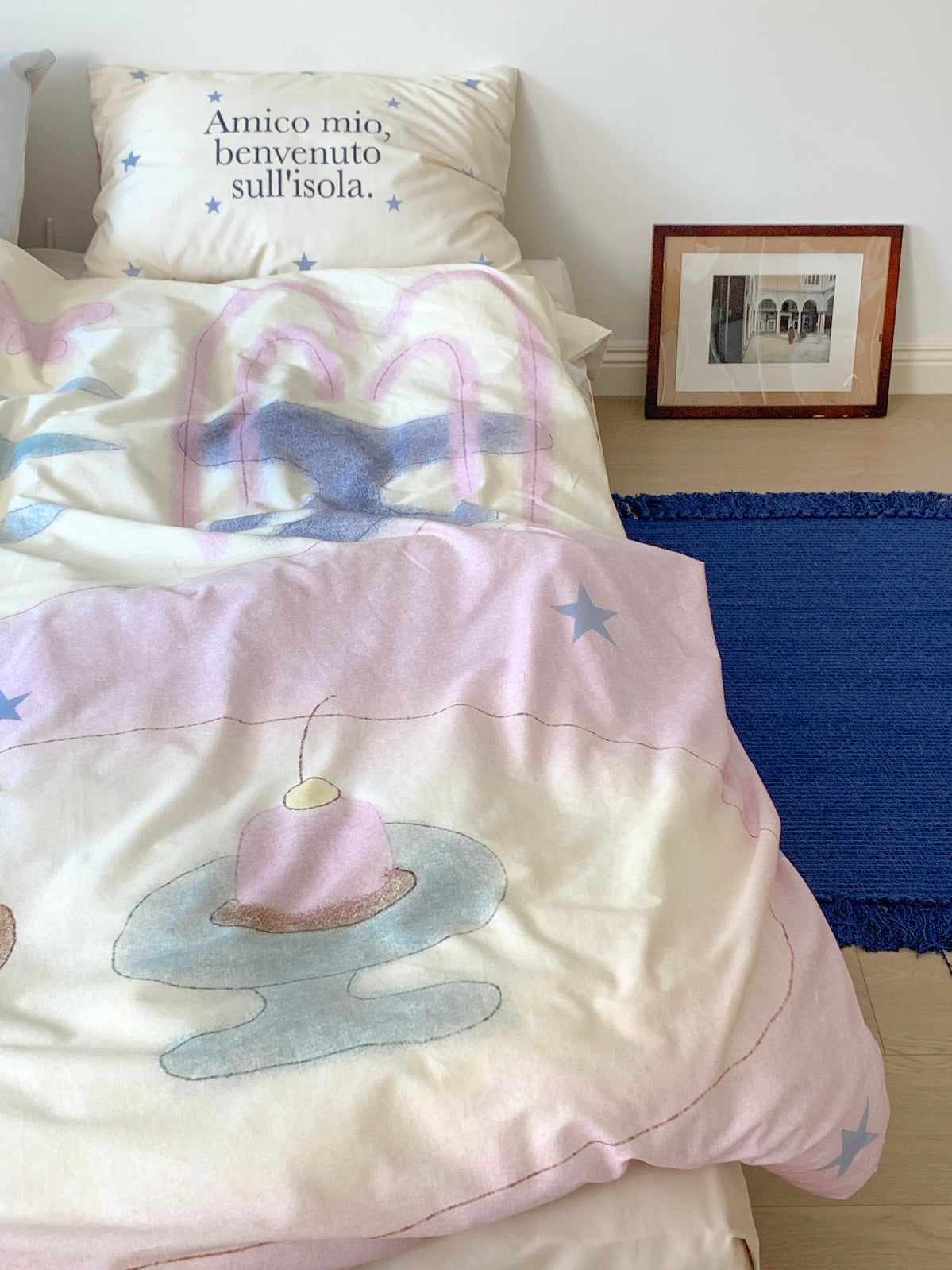 Pastel duvet cover draped over the bed with a candle and stand motif near the edge.