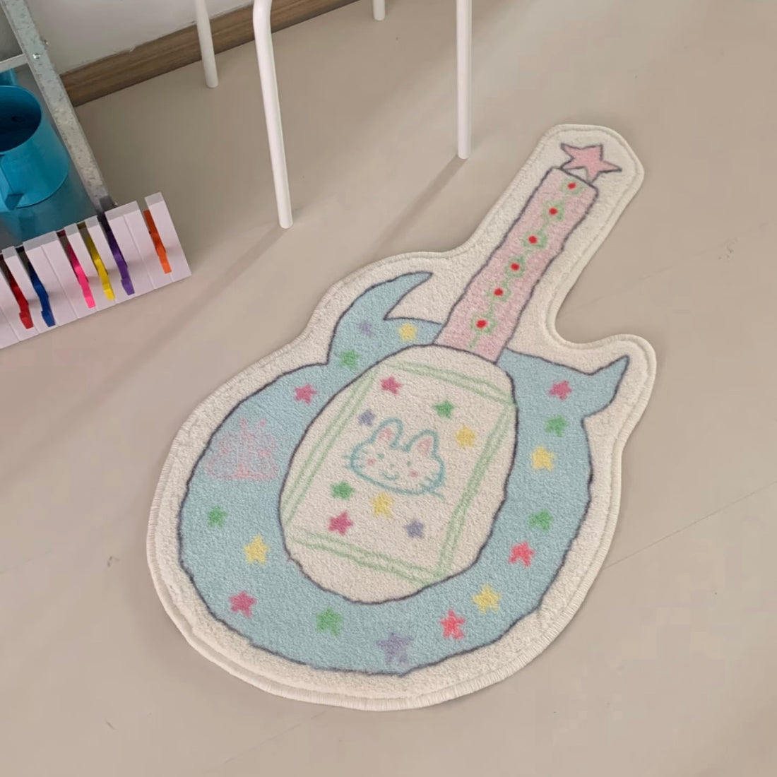 A guitar-shaped plush rug with a pastel bunny design, displayed on a light beige floor next to a pink mirror frame.