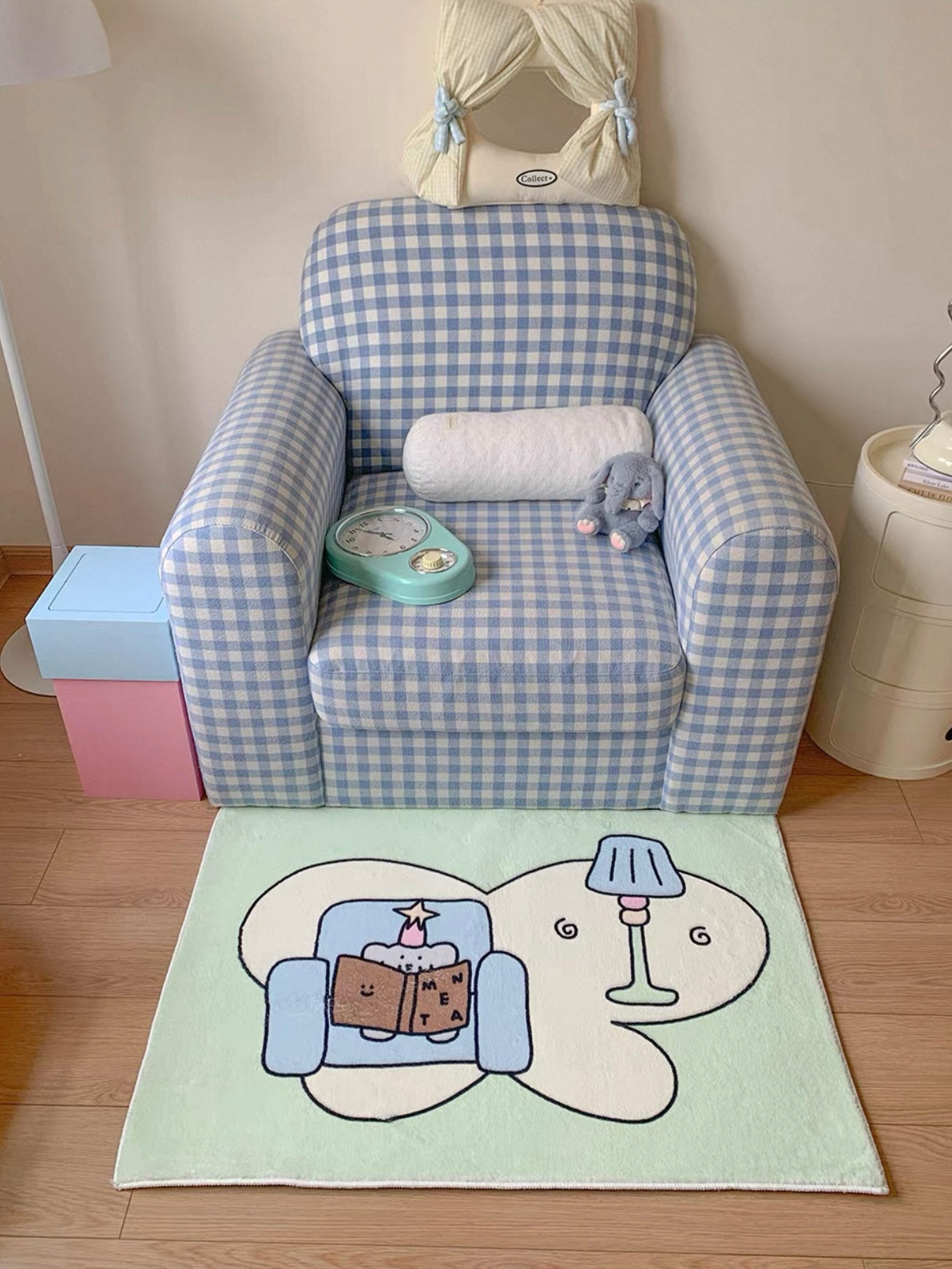 A pastel Kawaii rug in pale green lies in front of a checked armchair, with a reading elephant at its center.