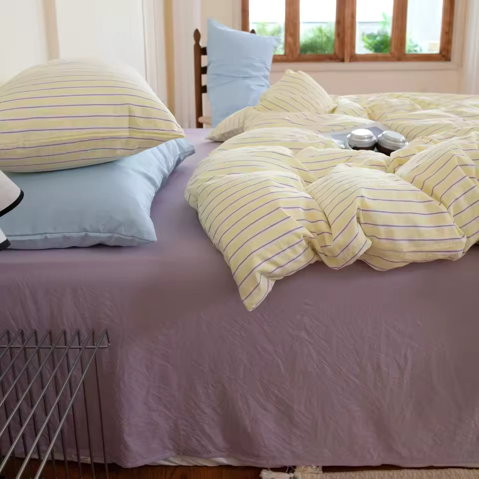 Bed with yellow striped bedding and light blue pillows in a room with a window.
