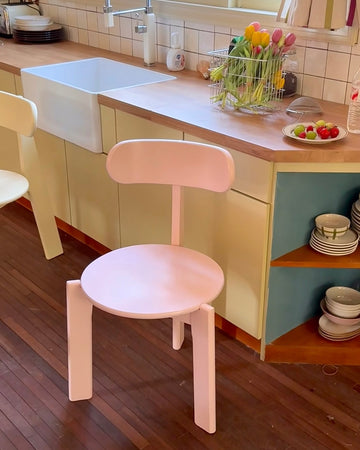 Pink chair in a kitchen setting with a wooden floor and colorful decor.