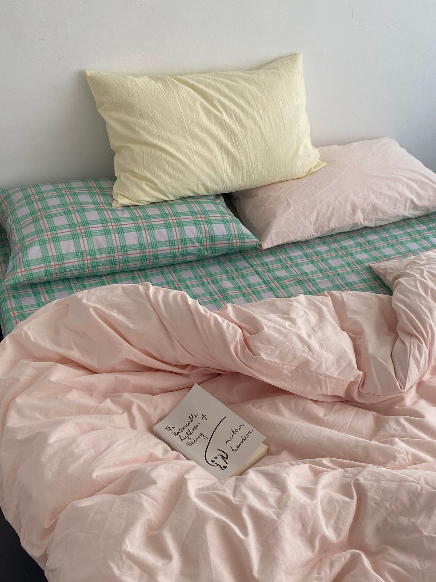 Bed with pink checkered duvet and pillows against a white wall