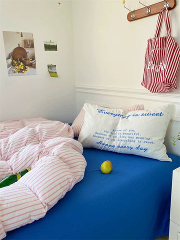 Bedroom with pink striped bedding, blue blanket, and pillows with text.