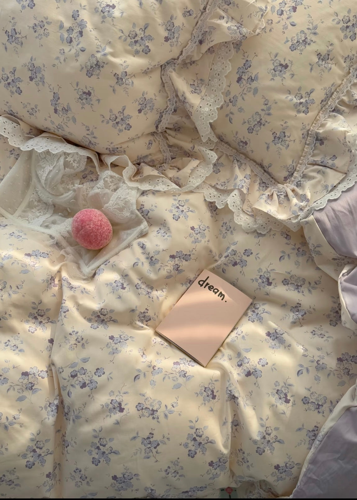 Floral patterned comforter with a pink ball and a small book on a bed.