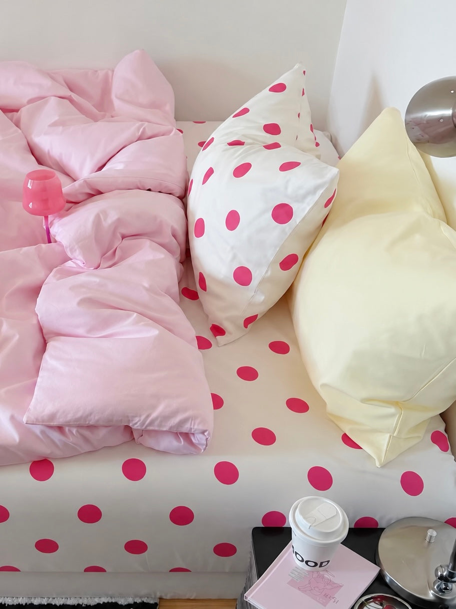 Pink cotton bedding with a pale yellow pillowcase and a white pillowcase with fuchsia dots above the dotted sheet.