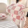 Person holding a pink and white checkered blanket in a cozy room.