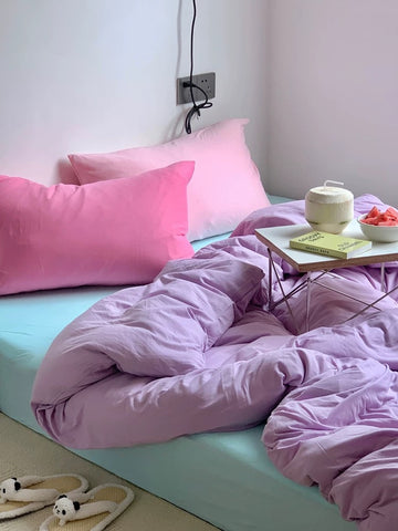 Bed with pink bedding and pillows, a small table with a teapot and bowl on a light blue bedspread.