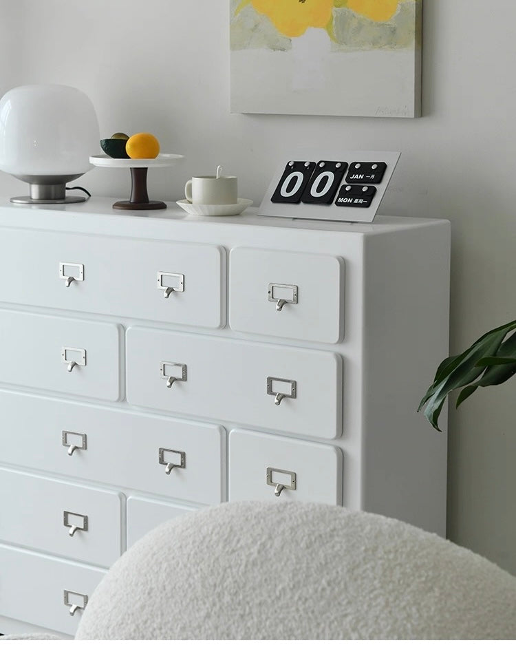 White dresser with decorative items including a clock and small plant, against a light gray wall.