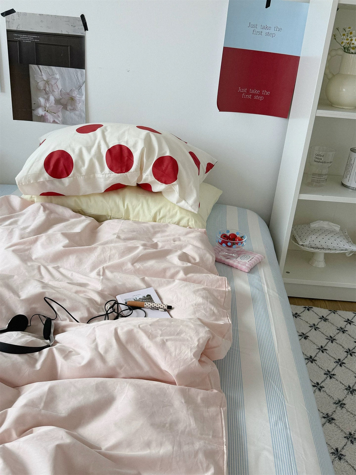 Large red dots and a yellow pillowcase sit at the head of a pink bed with striped sheet.