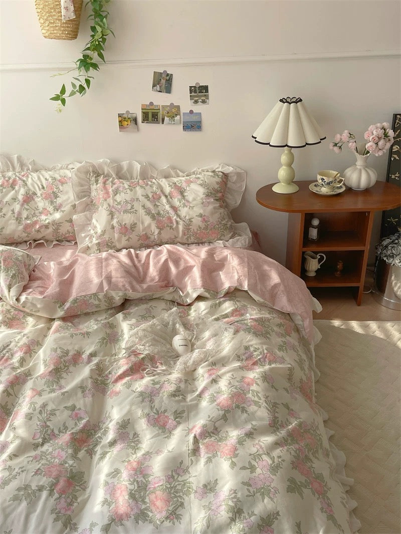 Floral bedding set on a bed in a bedroom with a lamp and window in the background.
