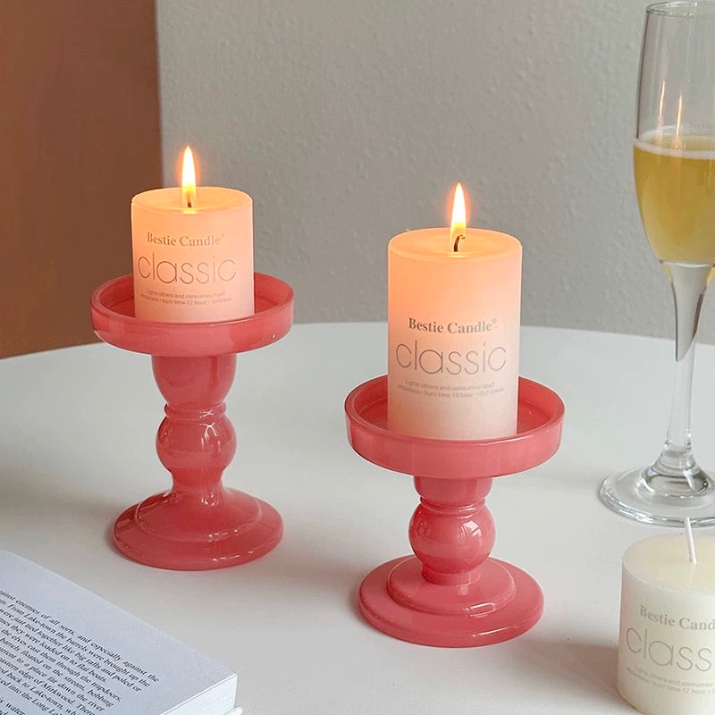 Two lit candles in pink holders on a table with a glass of champagne.
