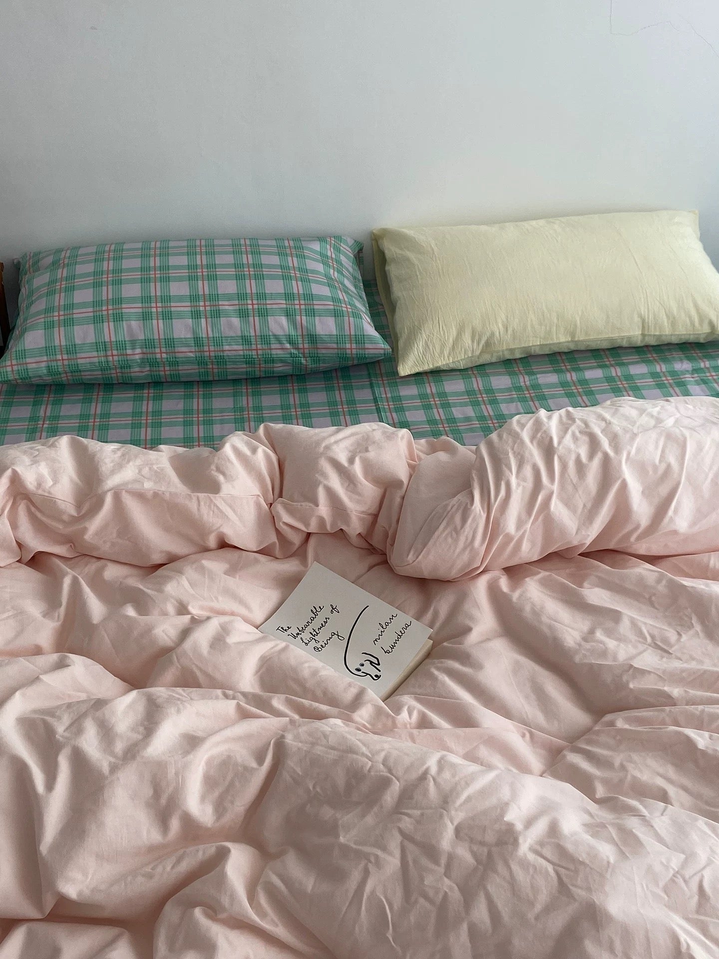 Pink comforter with a tag on a bed with green and white checkered sheets.