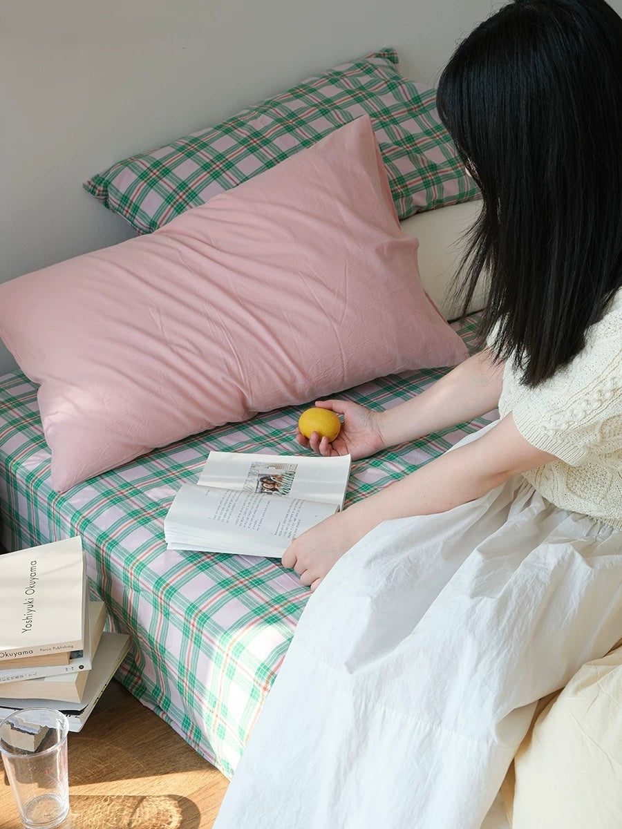 Person sitting on a bed with pink and green checkered bedding, holding a lemon.