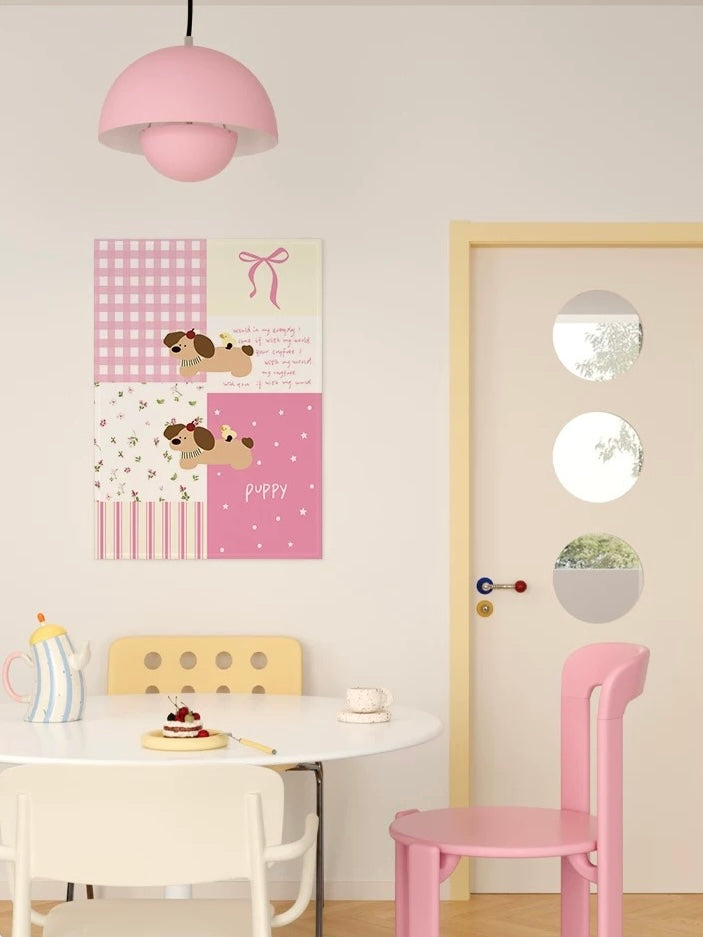 A pink patchwork puppy tapestry hangs above a small dining table, with a pink chair visible beside the door.