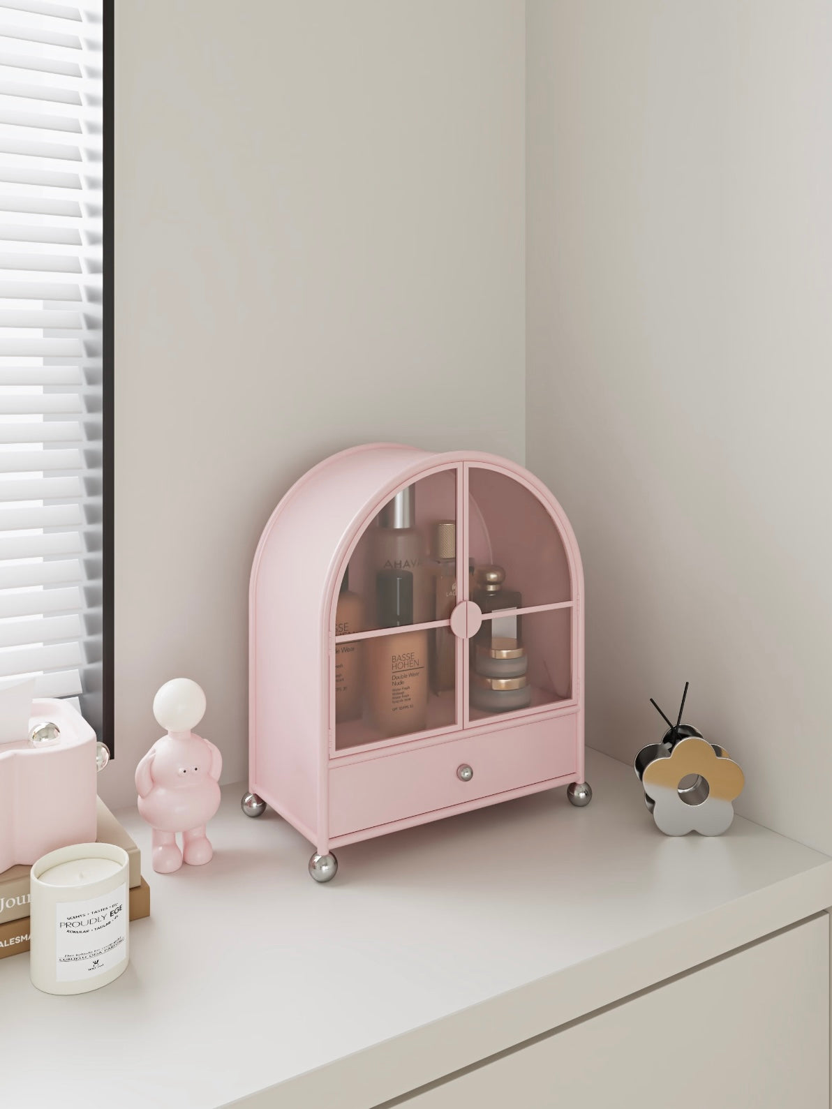 A pink perfume cabinet shown closer holds bottles and stacked cream jars behind its arched glass doors.