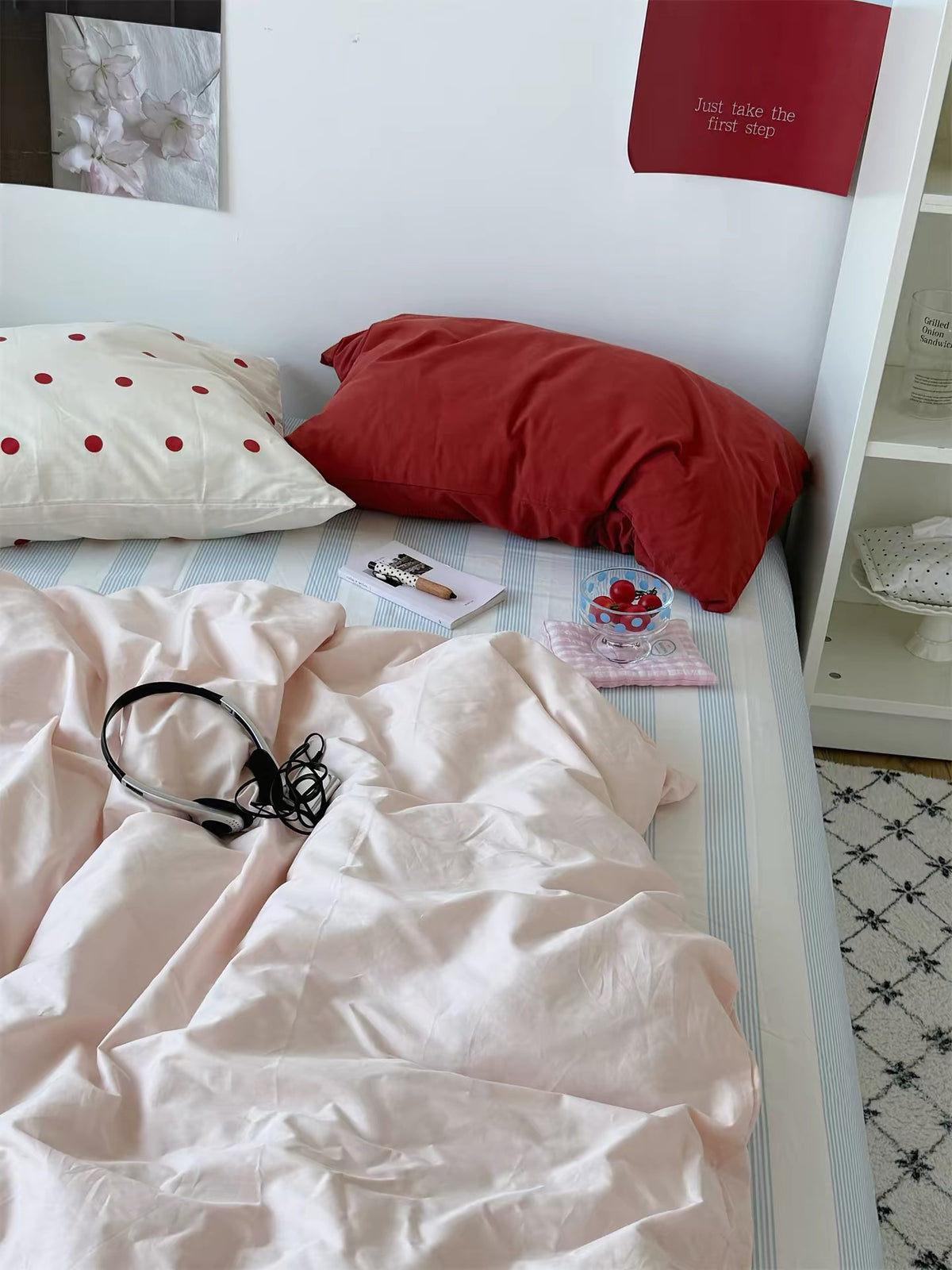 Pink preppy bedding with a red pillow and small red dot pillowcase above a blue striped sheet.