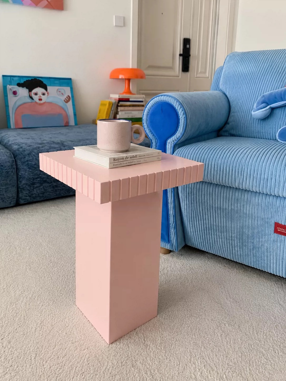 Pink small side table with a checkered mug beside a blue corduroy sofa