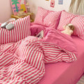 Pink and white striped bedding set on a bed with pillows and a teddy bear.