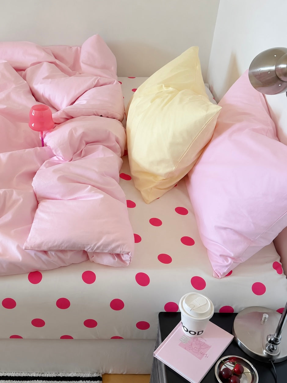 Pink and yellow solid pillowcases above a pink duvet cover and a white sheet with fuchsia dots.
