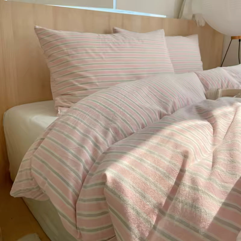 Pink and white striped bedding on a bed with a wooden headboard.