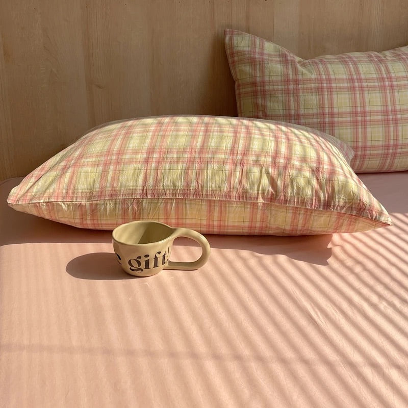 Plaid pillows on a bed with a ceramic mug labeled 'gift' in the foreground.