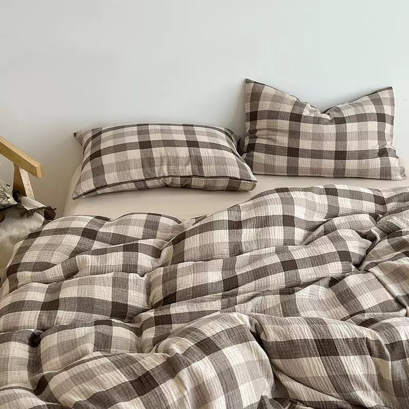 A bed made with a soft, textured plaid bedding set in brown, beige, and off-white. The set includes a duvet cover and two matching pillowcases, styled in a cozy bedroom setting against a plain light gray wall.