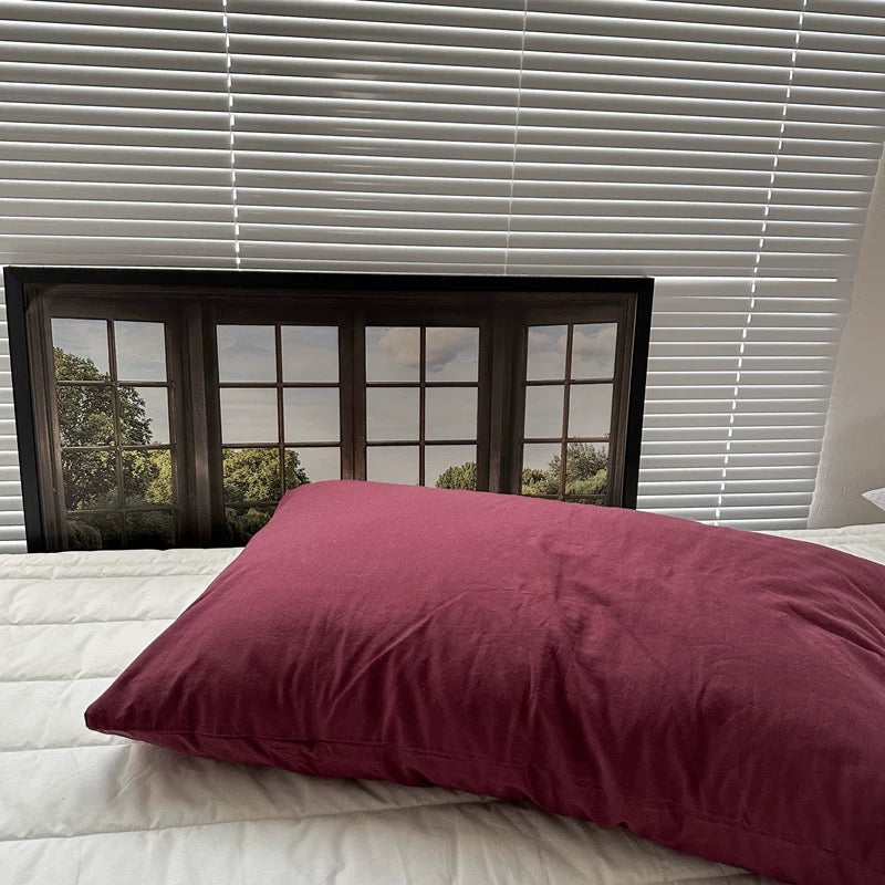 A plum pillowcase rests on white bedding beneath a framed window print.