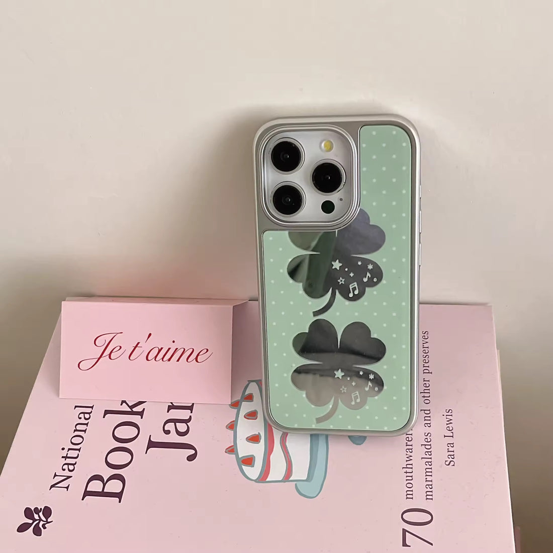 Coquette tech accessory featuring green clover charm and metallic frame iPhone cover