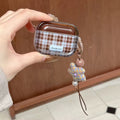 Hand holding a plaid airpod case with a decorative charm against a wooden background