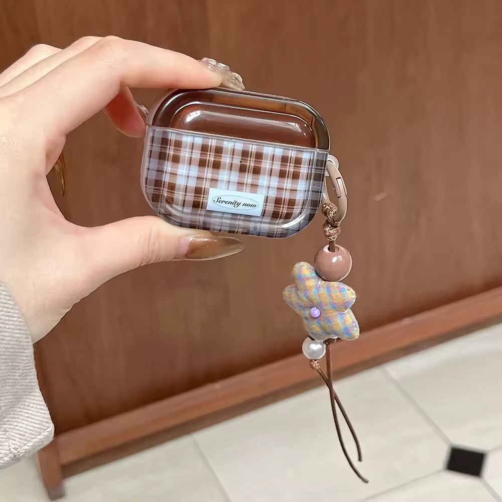 Hand holding a plaid airpod case with a decorative charm against a wooden background