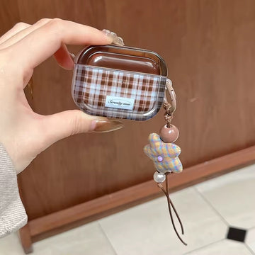 Hand holding a plaid airpod case with a decorative charm against a wooden background