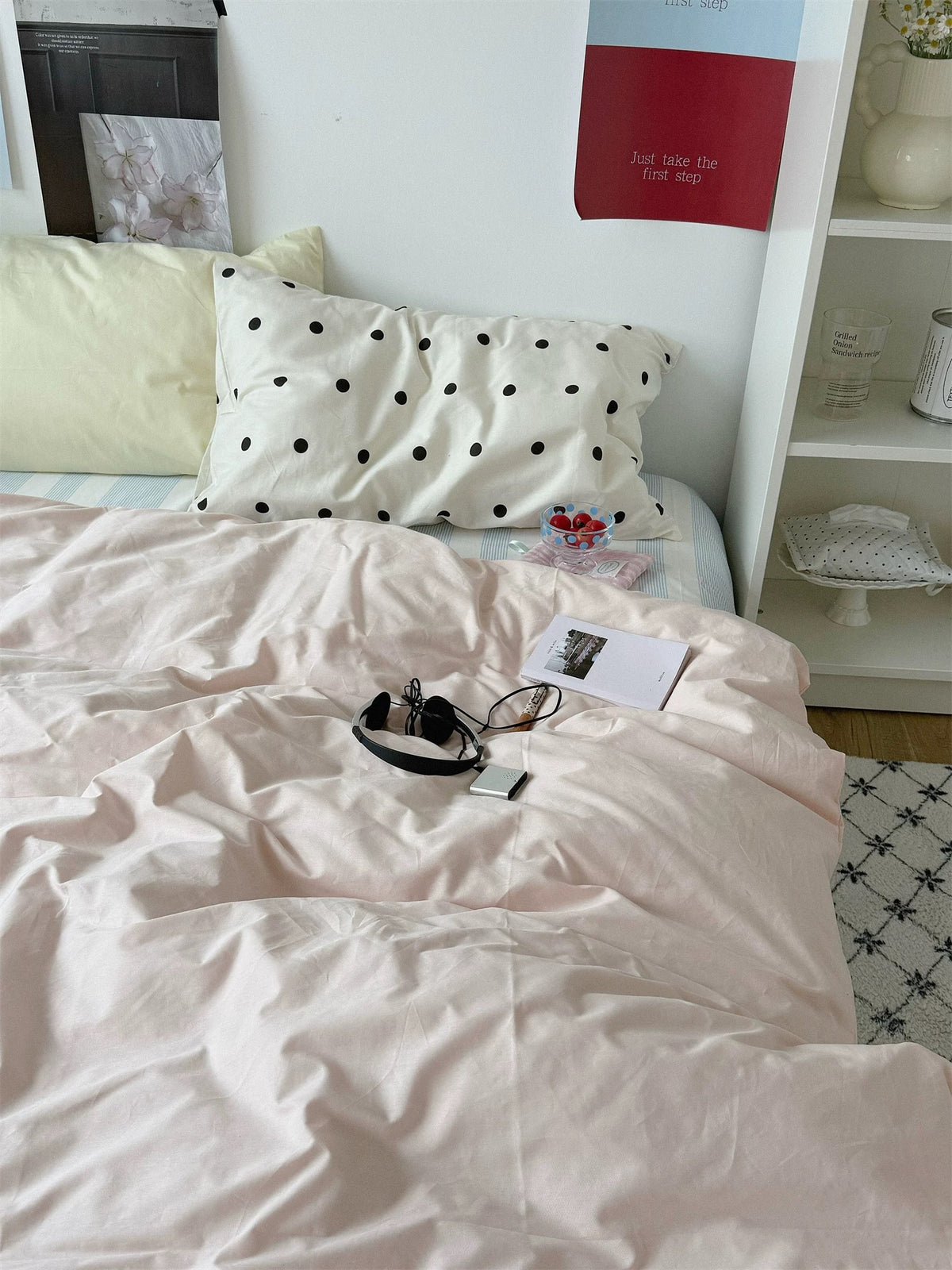 A yellow pillow and small black dot pillowcase sit above a pink duvet cover in a preppy bedroom.