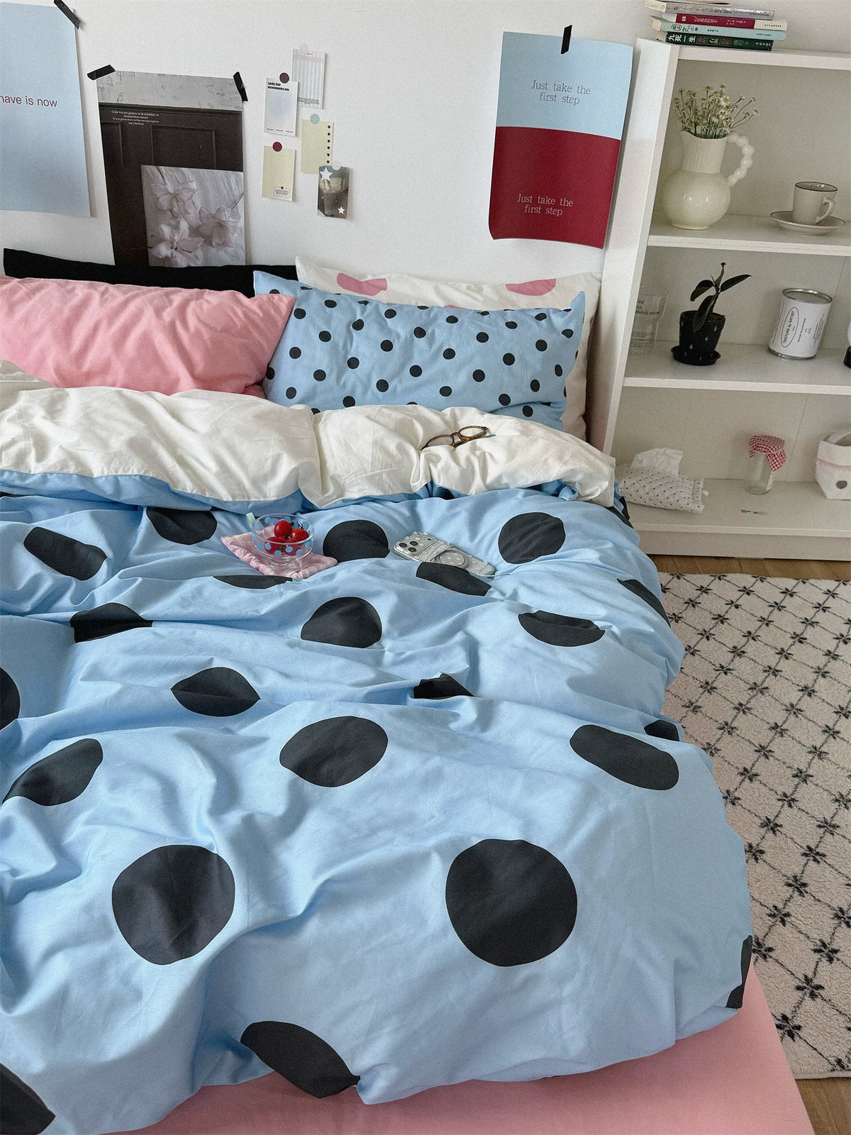 A full front view shows blue dotted bedding, a pink sheet and contrasting pillows beneath framed wall prints.