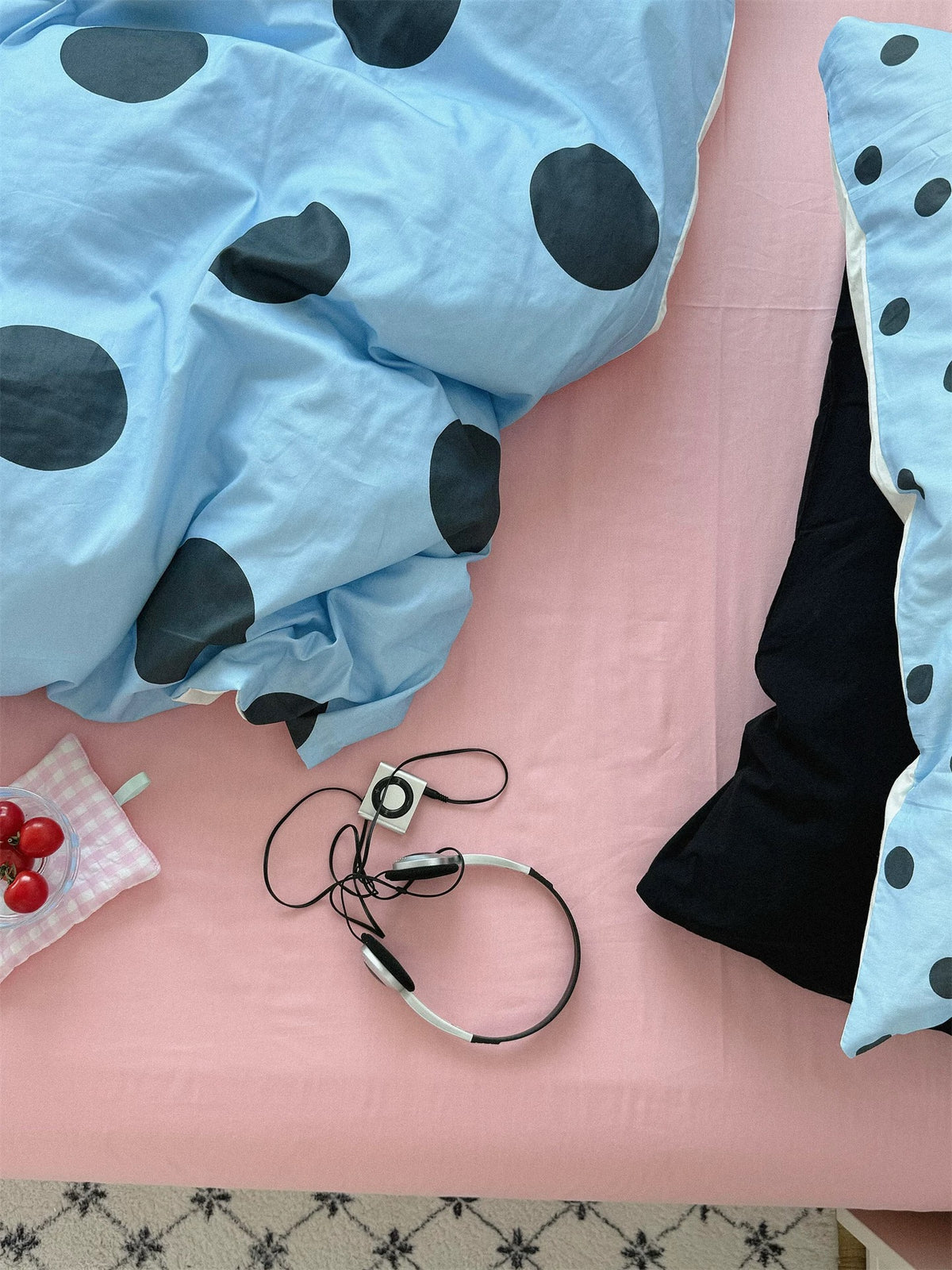 Preppy blue polka dot bedding set shown close up, with large black dots over a pink flat sheet and a black pillow beside it.