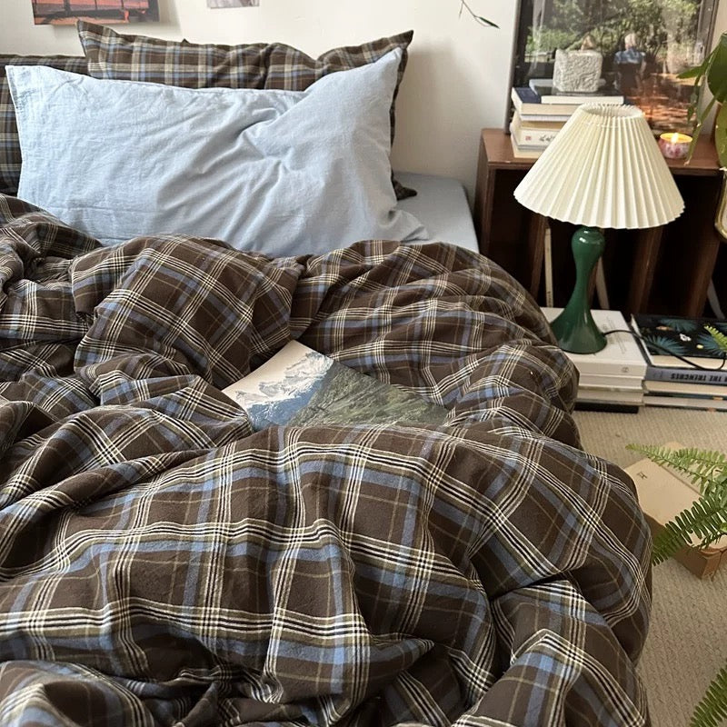 Bed with plaid bedding and pillows, surrounded by books and decor items.