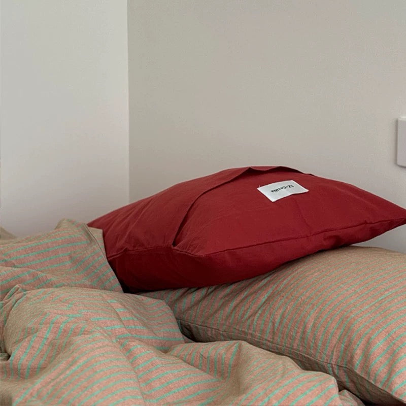 Red pillow on a bed with striped bedding against a plain wall
