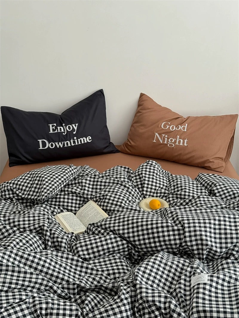 Bed with checkered duvet, pillows with text, and a book on a white background