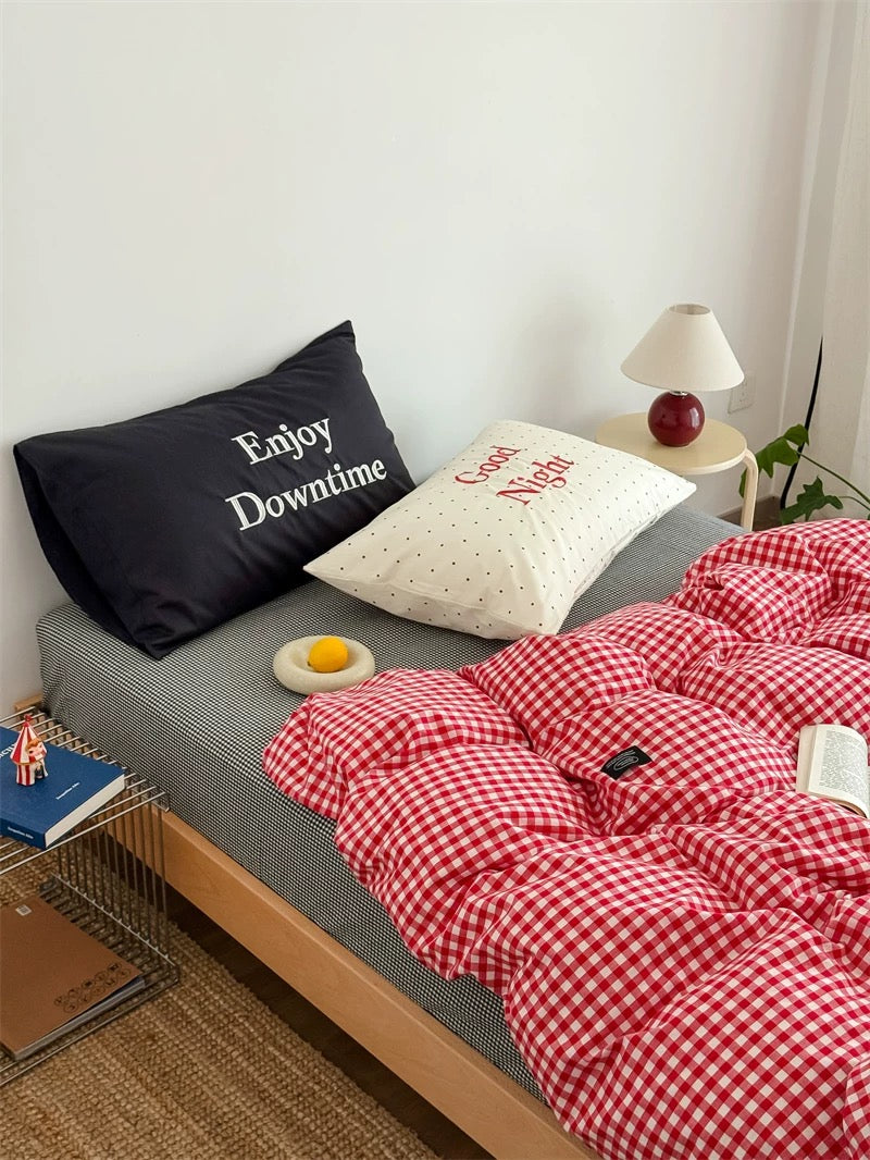 Bed with red checkered duvet, black pillow with 'Enjoy Downtime' text, and white pillow with 'Good Night' text.