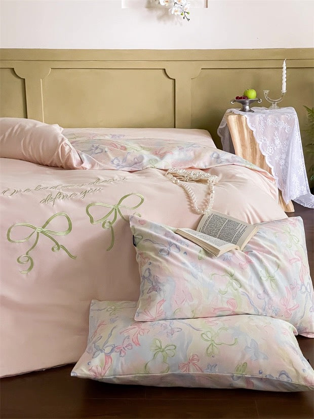 Pastel-colored bedding set with floral and bow designs on a bed.