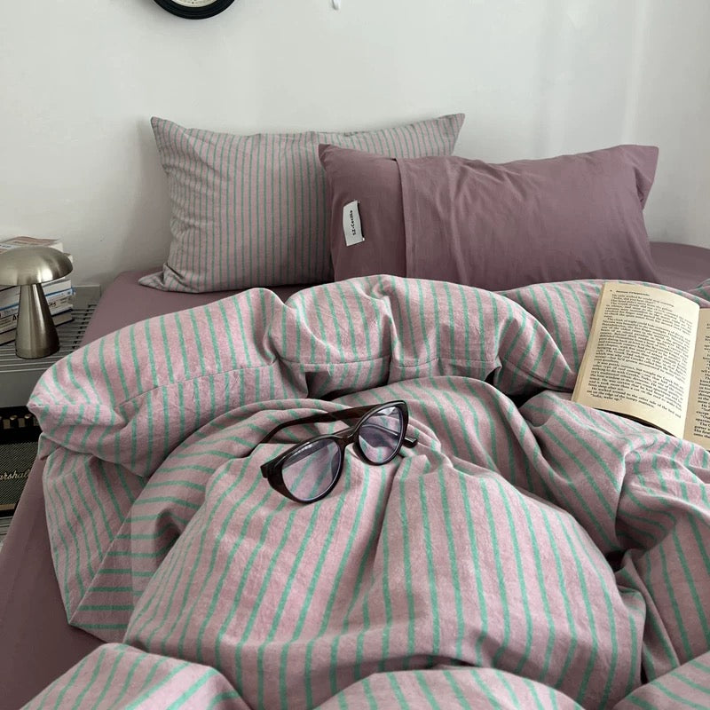 Bed with pink and green striped bedding, glasses, and a book on a white wall background.