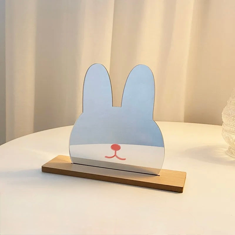 A minimalist bunny-shaped tabletop decor piece with a light blue upper half, white lower half, and a small red nose detail, standing on a rectangular wooden base on a white table.
