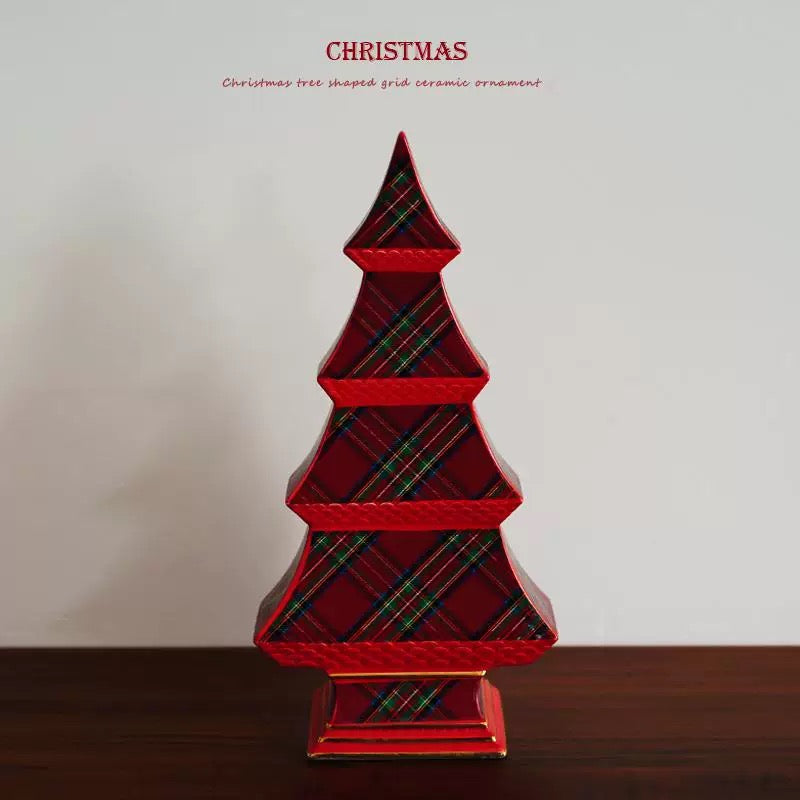 A red Christmas tree decoration stands on a tabletop, showing its plaid front and gold colored base lines.