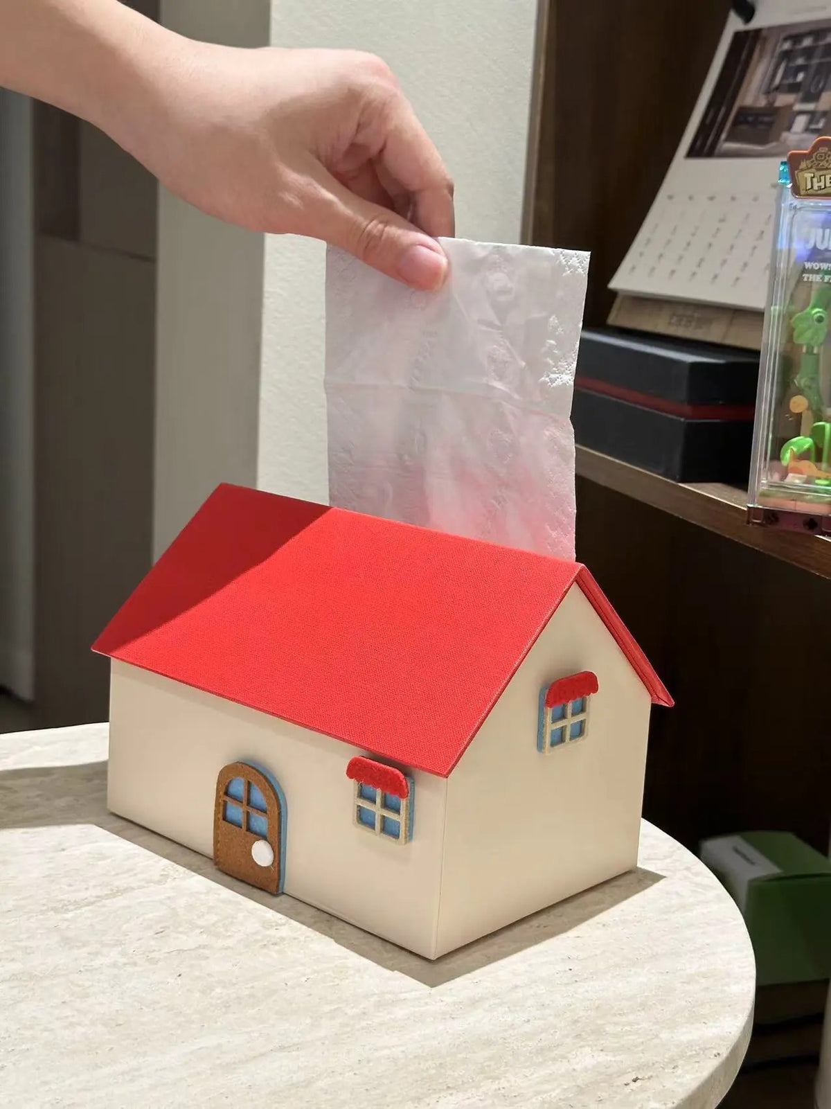 Red and cream house tissue box cover with tissue pulled through the roof opening