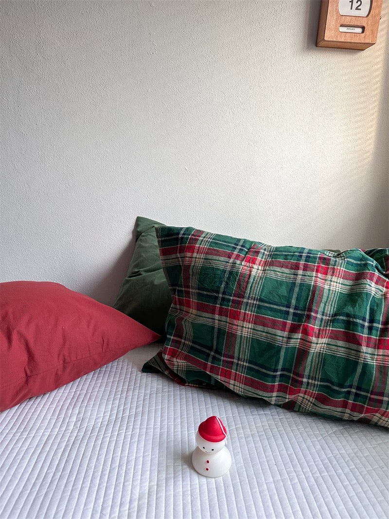 A red pillowcase lies beside a green and red tartan pillowcase.