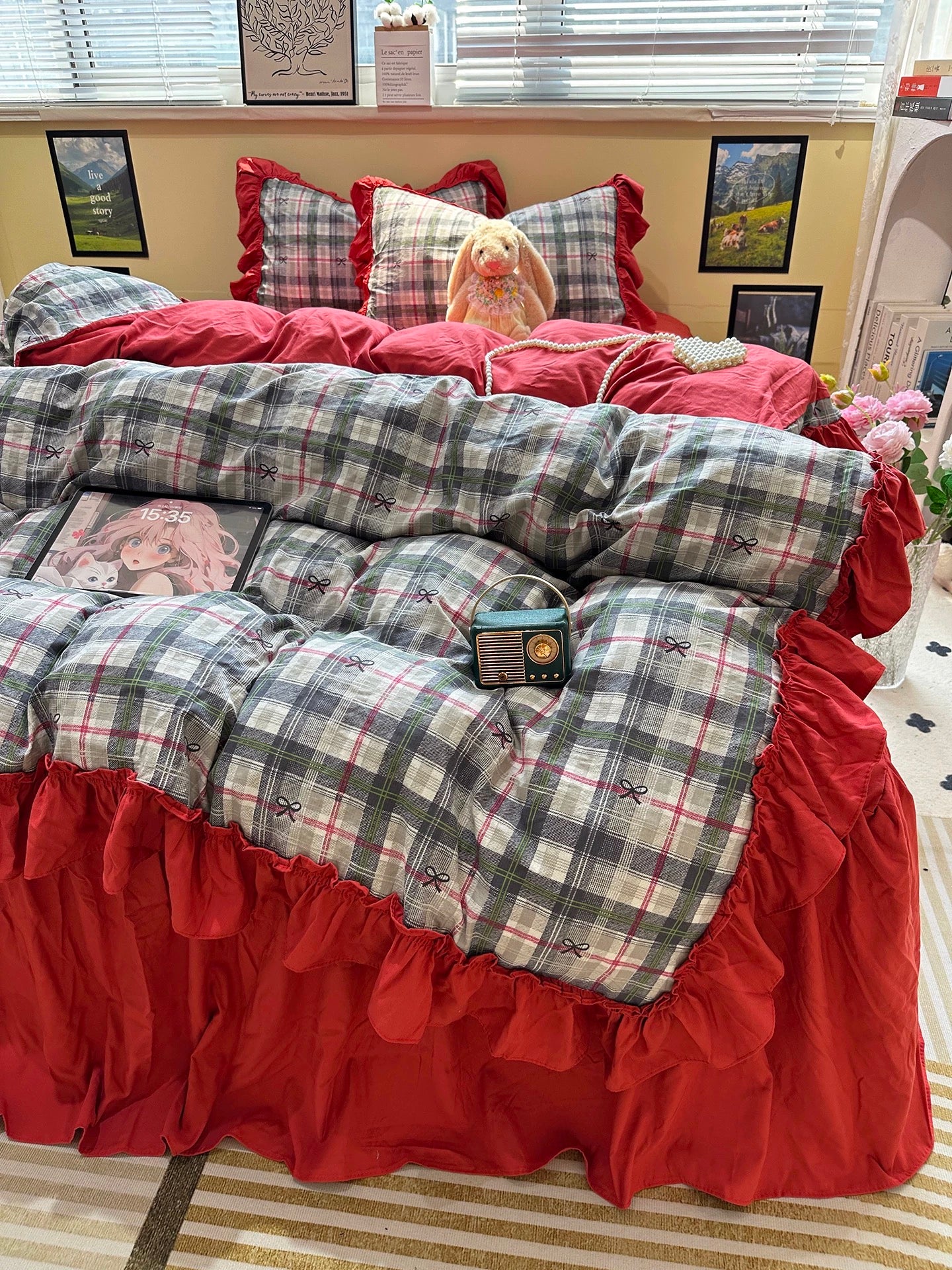 Bed with plaid bedding and red ruffled skirt in a room with pictures on the wall.