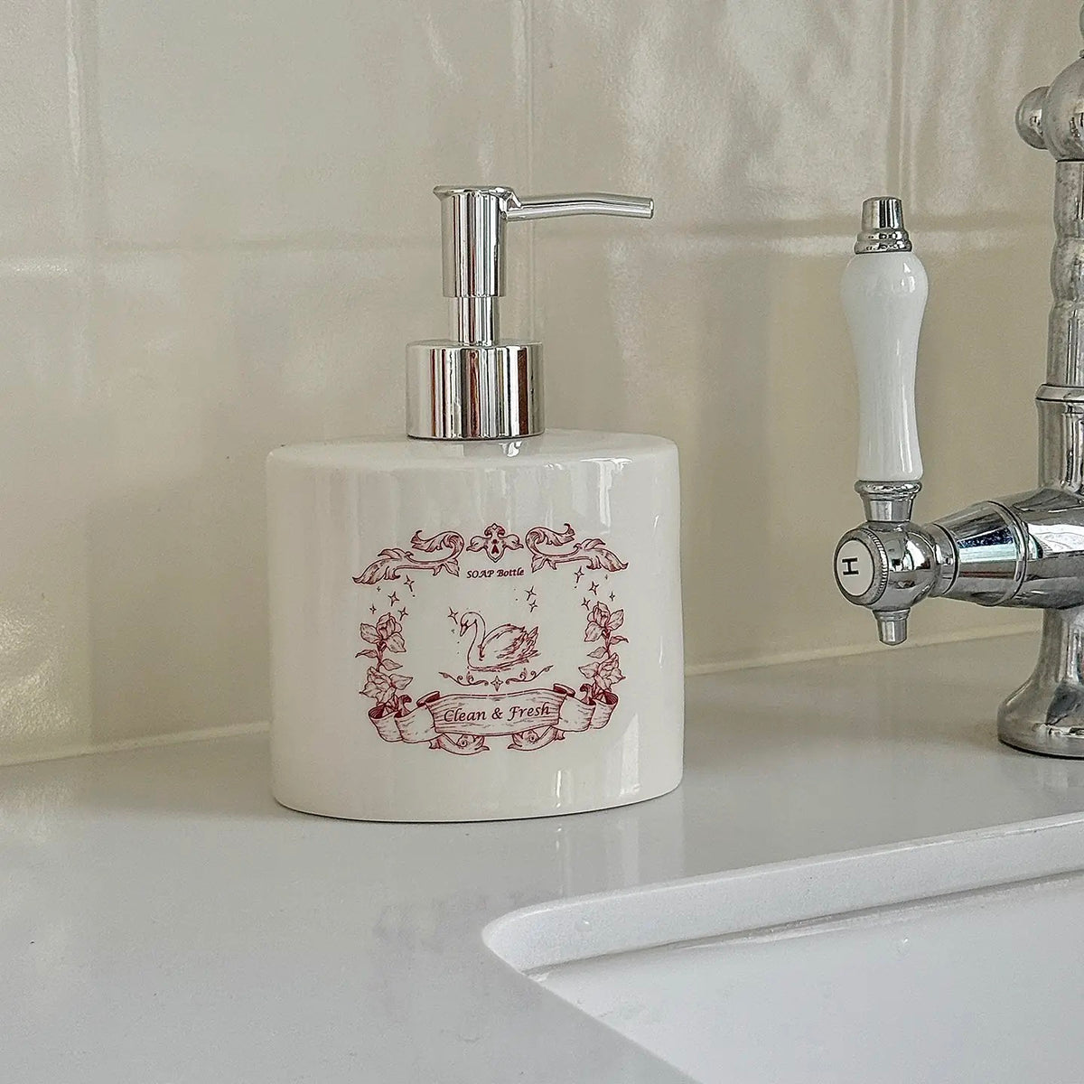 A red swan ceramic soap dispenser stands beside a faucet with its floral illustration facing forward.