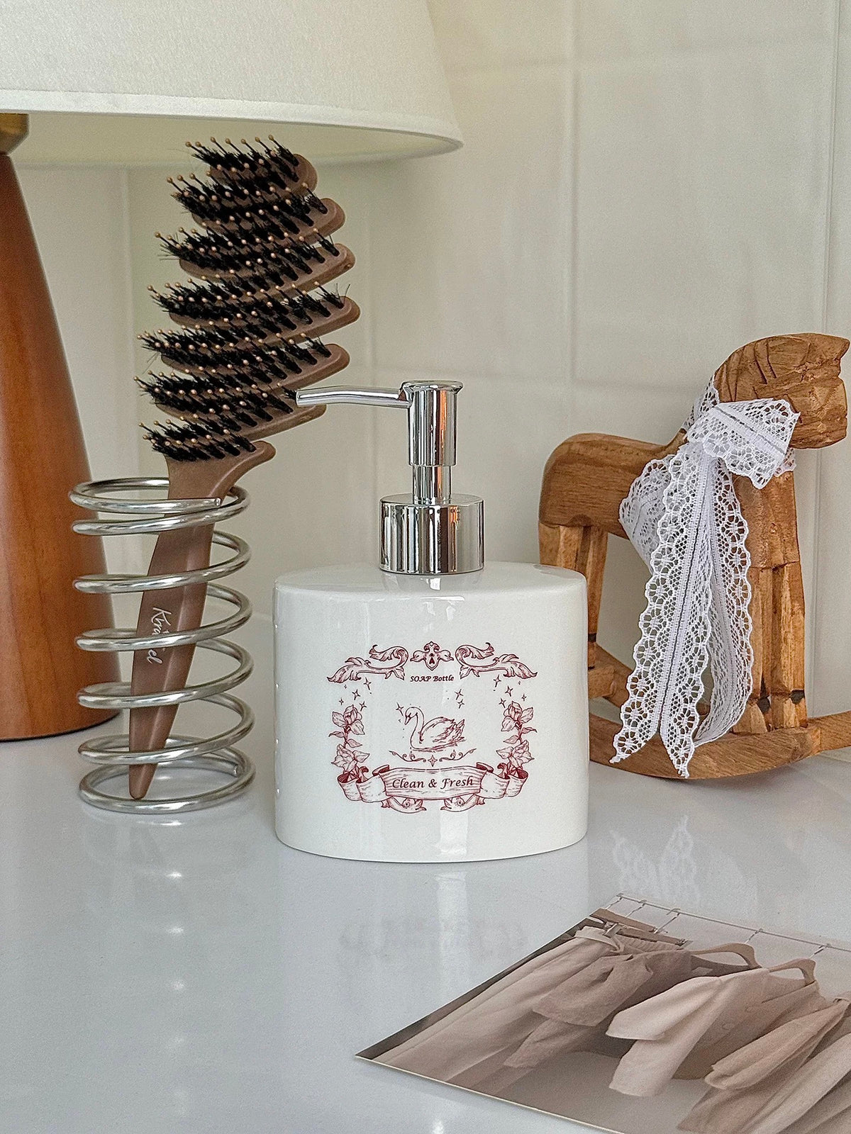 A white soap bottle with red swan artwork is shown from the front beside bathroom accessories.