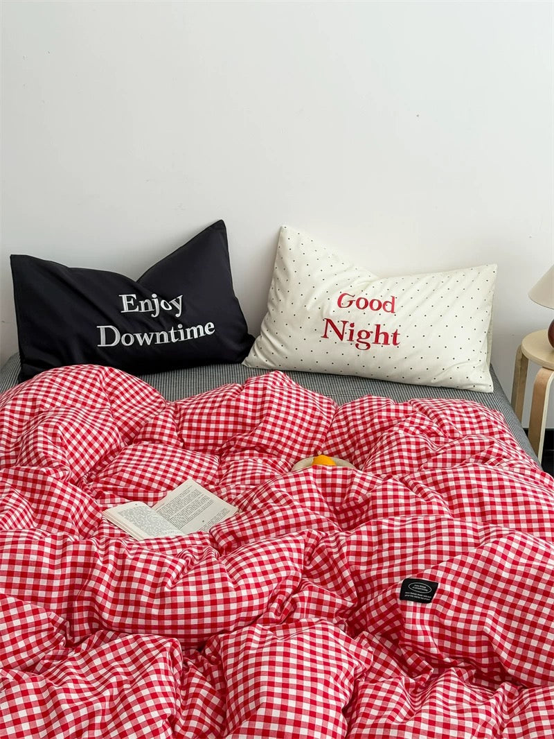 Red and white checkered duvet with two pillows, one black and one white, on a bed.
