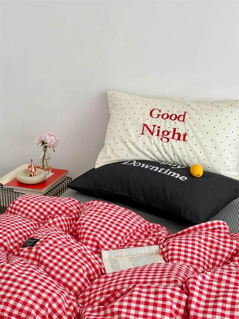 Bed with red and white checkered duvet, black pillow with 'Downtime' text, and white pillow with 'Good Night' text.