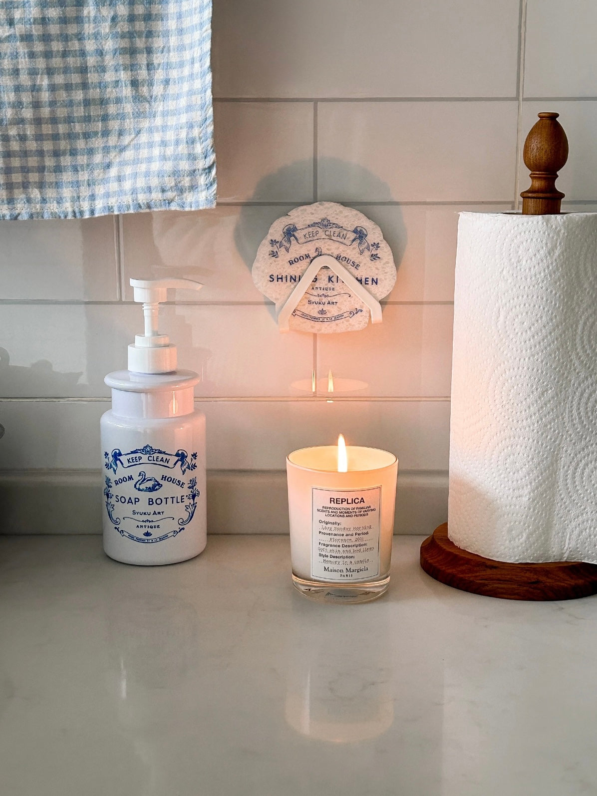 A refillable soap dispenser stands near a candle, with a matching swan sponge displayed above the bottle.